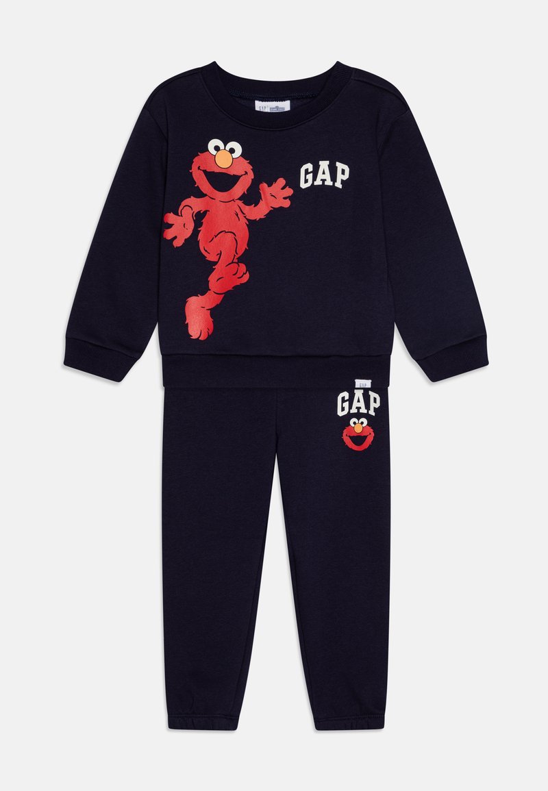 Marineblå pyjamas sæt lavet af bomuld. Har et rødt Elmo grafik på sweatshirt og bukser, med "GAP" tekst i hvid. Elastisk talje.