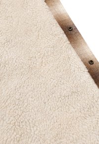 Tessuto in pelliccia color crema con una superficie strutturata e soffice. Un bordo decorato di colore marrone con bottoni metallici corre lungo un lato.