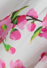 Gros plan sur un tissu blanc à imprimé floral rose avec des boutons, des pétales et des feuilles vertes.