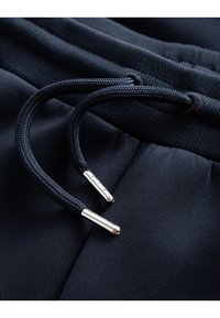 Navy drawstring with black braided cord and silver metal aglets, attached to a soft, smooth fabric waistband.