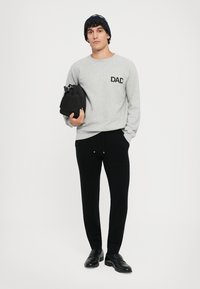 Sudadera gris con "DAD" impresa en el pecho, combinada con pantalones deportivos negros y mocasines negros, sosteniendo un bolso negro. Gorro de punto texturizado.