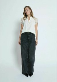 Hvid bluse med blondesæde og V-hals, parret med højtaljede, brede sorte denimjeans. Minimalistiske accessories er synlige.