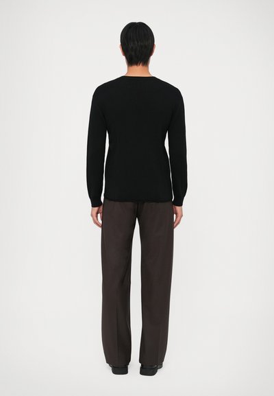 Sweater preto canelado de manga longa com decote arredondado, combinado com calças largas castanho-escuras, visto de costas.