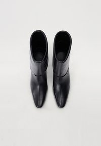 Bottines en cuir noir avec un bout pointu, un design à rabat et une texture lisse. Silhouette minimaliste, sans matériel ou accents visibles.