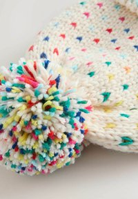 Knit hat made of soft, cream-colored yarn, featuring multicolored speckles and a large, fluffy pom-pom at the top.