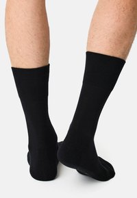 Calcetines de algodón negros con puños acanalados, que presentan una textura suave y una longitud estándar hasta el tobillo, mostrando una vista ampliada del tobillo y el pie.