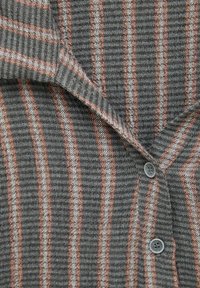 Gros plan sur un tissu gris à rayures verticales marron et blanches, montrant le col et deux boutons gris sur une veste ou une chemise texturée.