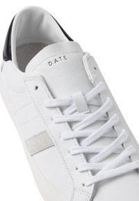 Sneaker in pelle bianca con tallone nero, accento in suede grigio e lacci bianchi. Presenta logo impresso e texture liscia.
