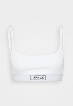 White cotton bralette with slim straps and a wide elastic band featuring a black "VERSACE" logo in a rectangular patch.