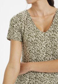 Short-sleeve dress in olive green with a v-neck, featuring a white floral pattern throughout. Soft fabric with a relaxed fit.
