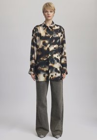 Camicia con bottoni in un motivo tie-dye di nero, beige e marrone, abbinata a jeans grigi a vita alta e a gamba larga. Tessuto morbido, vestibilità comoda.