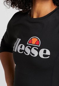 Czarna koszulka sportowa z rękawami do trzy czwarte, okrągłym dekoltem oraz wyraźnym szarym logo z wielokolorowym emblematem powyżej.