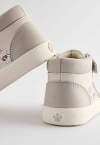 Baskets montantes gris clair avec une texture lisse, présentant un imprimé de cartoon vibrant sur le côté et un logo de patte sur le talon.