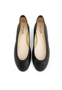 Des chaussures plates noires avec un motif texturé en nid d'abeille, des bords élastiqués et une semelle plate. L'intérieur présente une doublure beige neutre.
