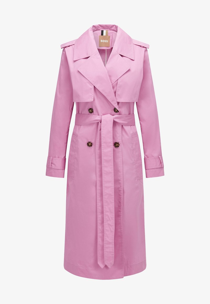 Long trench-coat rose à double boutonnage avec ceinture, col à revers, épaulettes et poignets boutonnés, présenté sur fond blanc.