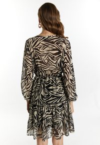 Rochie stratificată neagră și bej, cu mâneci lungi, având un design cu imprimeu zebra și o talie elastică pentru o siluetă ajustată.