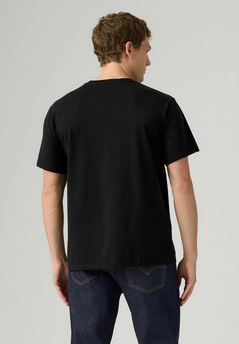 Maglietta nera in cotone con maniche corte, scollo a girocollo e rifinitura pulita. Indossata con jeans blu scuro, presenta un design posteriore semplice.