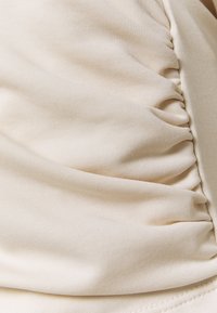 Beige tyg med sammangjorda, rynkade sömmar som skapar mjuka veck och textur på den släta textilytan.