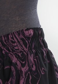 Joustovyötäröllinen hame mustana, jossa on abstrakti violetti marmoroitu kuvio. Kankaan pinta näyttää sileältä, kevyeltä ja hieman kiiltävältä.