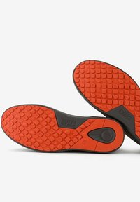 Suole di scarpe in gomma rosse e nere con motivo di presa testurizzato, caratterizzate da un logo in rilievo e dettagli di design circolare.