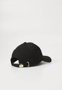 Black cotton cap with a curved brim, adjustable strap at the back with a gold-tone buckle, and subtle yellow accent under the brim.