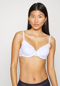 Bílé podprsenka s krajkovým lemem, tvarované košíčky a nastavitelné ramínka, s hladkým povrchem a jednoduchým, klasickým designem.