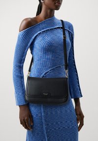 Black leather shoulder bag with a textured finish, featuring silver-tone hardware and a flap closure. Worn crossbody with adjustable strap.