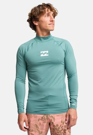 Koszulka do surfowania z długim rękawem w kolorze morskim, z wysokim kołnierzem i białym logo fali na piersi. Wykonana z gładkiego, elastycznego materiału.