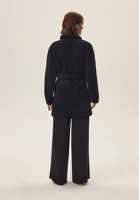 Czarny szlafrok z polaru o teksturowanej powierzchni, z długimi rękawami, kołnierzem szalowym i pasującym paskiem z tego samego materiału, sięgający do połowy uda.