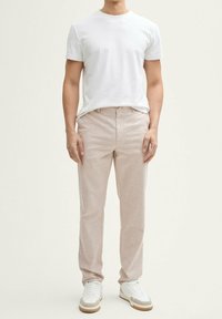 Camiseta blanca de cuello redondo, pantalones tejidos en tono beige claro y zapatillas blancas con acentos beige, todo de corte casual.