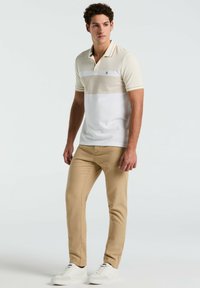 Korte mouwen polo in een crème en beige kleurblok, met een gestructureerde bovenkant, een tweeknoopsluiting en een contrasterende kraag met strepen. Tan-pantalon, witte sneakers.