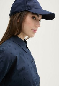 Navy cap with embroidered logo, paired with a navy button-up shirt featuring textured patterns and a classic collar.