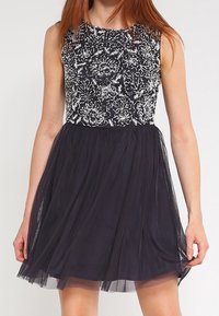 Sleeveless dress with a fitted, embellished bodice featuring floral patterns in silver on a black background, flowing black tulle skirt.