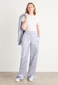 lichtblauwe cargobroek met wijde pijpen, voorzien van voorzakken en een taillering, gecombineerd met een wit poloshirt en een grijze blazer.