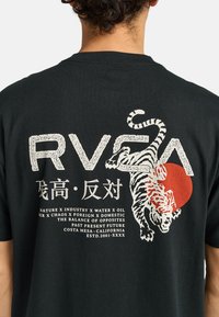 Černé bavlněné tričko s grafikou bílé tygrice, červeným kruhovým prvkem a tučným bílým textem. Design obsahuje japonské znaky a podrobný text.