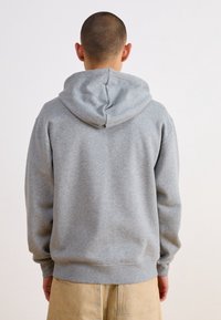 Felpa grigia in cotone con cappuccio, vestibilità rilassata, polsini e orlo a costine. Tessuto liscio, design minimal, appare casual e confortevole.