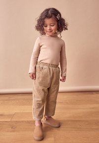 Beige bomulds langærmet top parret med lysebrune fløjlsbukser med lommer og blomsterbroderi, komplementeret af beige træsko.