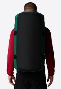 Sac à dos noir et vert en tissu durable, de forme rectangulaire, avec des bretelles réglables et des boucles latérales pour une fermeture sécurisée.