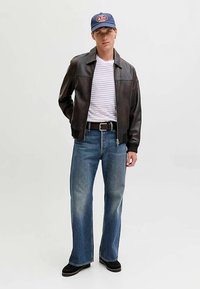 Bruine leren bomberjack, wit-grijs gestreept T-shirt, blauwe jeans met rechte pijpen, zwarte schoenen, blauwe pet met logo.