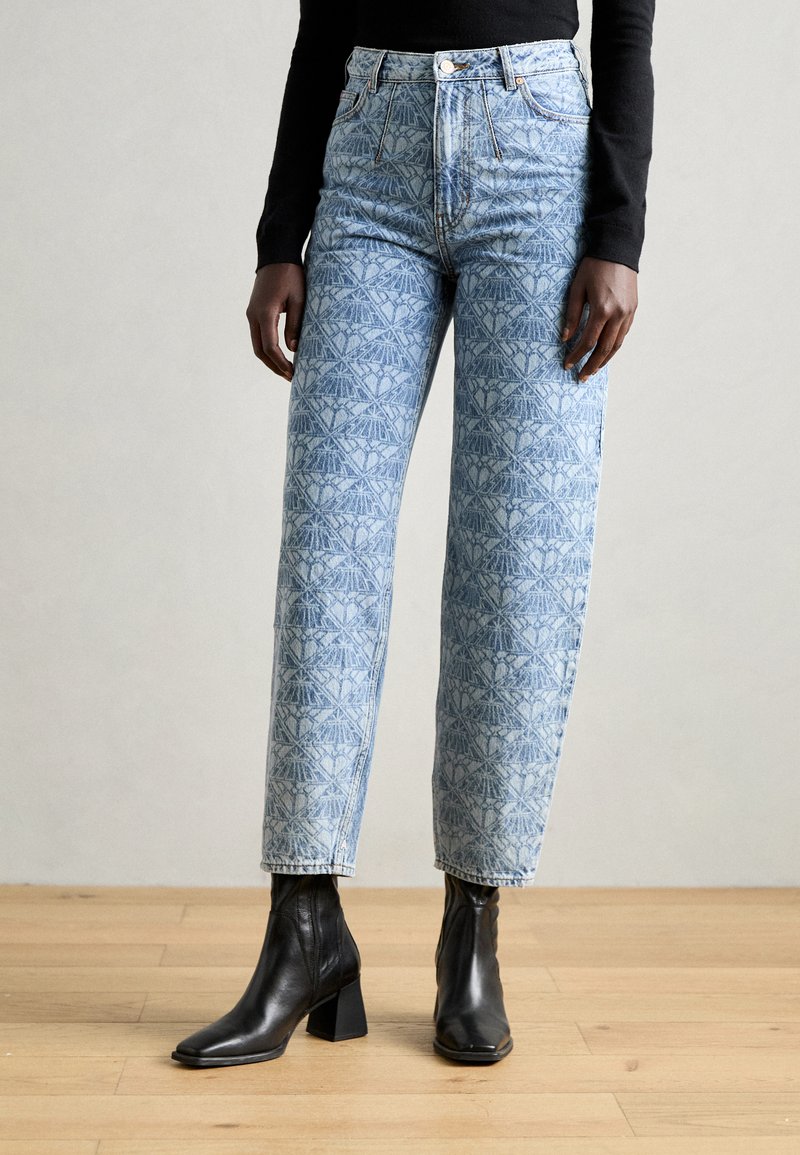 Light blue patterned denim jeans with a high waist, featuring a geometric design and straight-leg fit, paired with black ankle boots.