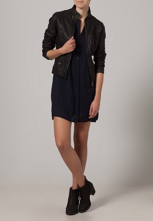 Black leather jacket with a zip front, worn over a dark blue shirt dress, paired with black ankle boots. Smooth texture, fitted design.