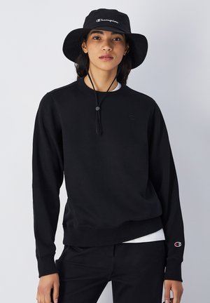 Sudadera negra con cuello redondo, puños y dobladillo de canalé. Presenta un pequeño logotipo negro en el pecho y un logotipo rojo y blanco en la manga.