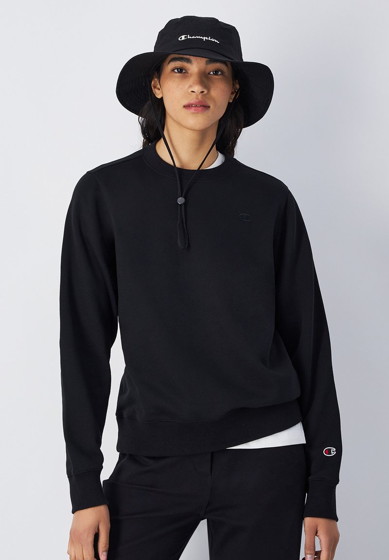 Sudadera negra con cuello redondo, puños y dobladillo de canalé. Presenta un pequeño logotipo negro en el pecho y un logotipo rojo y blanco en la manga.