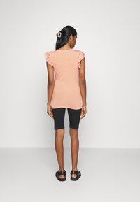 T-shirt às riscas em laranja e branco com mangas franzidas, combinado com calções pretos e sandálias pretas, visto de costas contra um fundo liso.