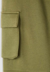 Materiał bluzy w kolorze oliwkowej zieleni o teksturowanym wyglądzie, z wyraźną naszywaną kieszenią z boku. Prosty, funkcjonalny design.