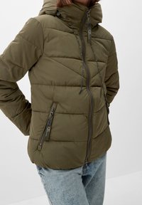 Olive green puffer jacket with horizontal stitching, a hoodie, and two zippered side pockets. Features a front zipper with toggle adjustments.