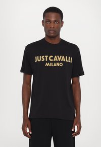 Černé bavlněné tričko s velkým zlatým nápisem "JUST CAVALLI MILANO" na přední straně. Krátké rukávy a kulatý výstřih.