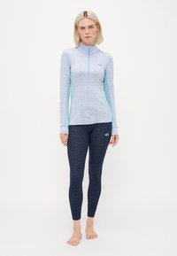 Langermet lys blå rashguard med blomsterprint og halv glidelås; kombinert med marineblå leggings med små hvite detaljer. Glatt tekstur.