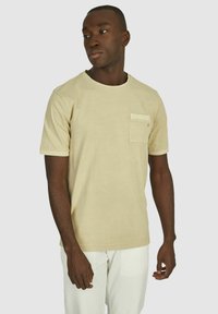 Beige t-shirt met korte mouwen, gemaakt van katoen, met een borstzak en een ronde hals. Gladde textuur met eenvoudige, strakke lijnen.