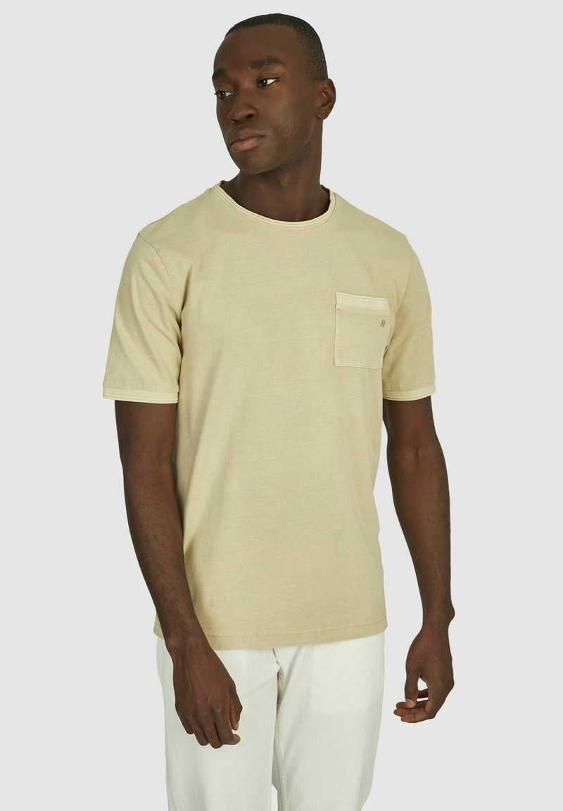 Beige t-shirt met korte mouwen, gemaakt van katoen, met een borstzak en een ronde hals. Gladde textuur met eenvoudige, strakke lijnen.